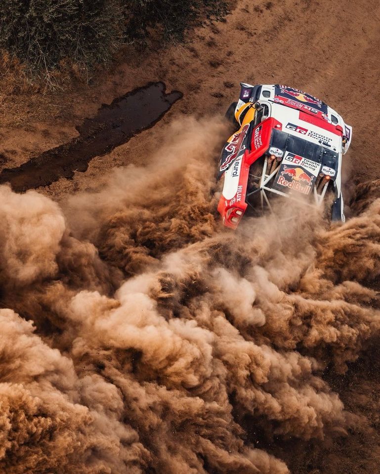 A photograph of a Redbull branded car drifting on a dirt road